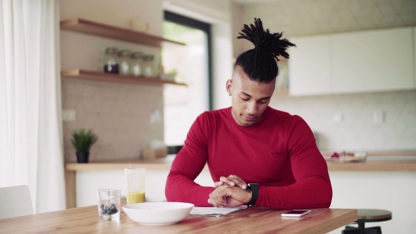 A mixed race young sporty man with smartwatch indoors at home, using smartwatch. Slow motion.