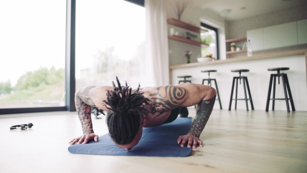 A mixed race young man with tattoo doing exercise indoors at home, a body workout. Slow motion.