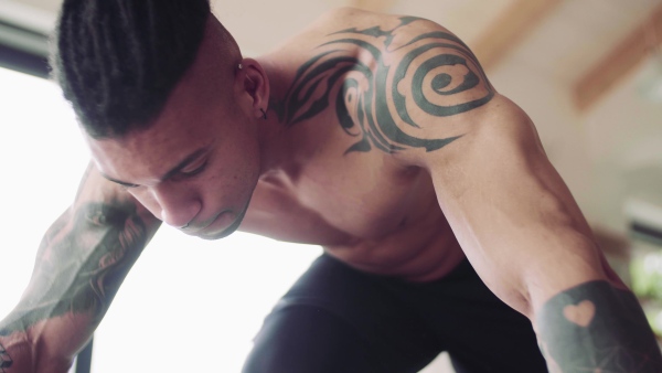 A mixed race young man with tattoo doing exercise indoors at home, a body workout.