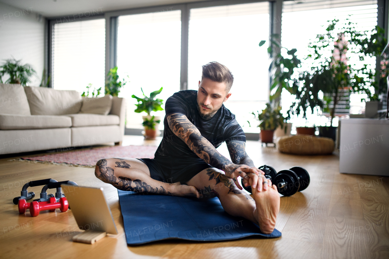 Front view portrait of young man with tablet doing workout exercise indoors at home.