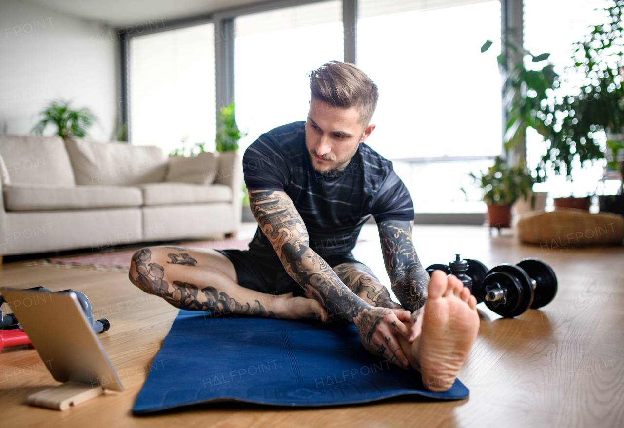 Front view portrait of young man with tablet doing workout exercise indoors at home.