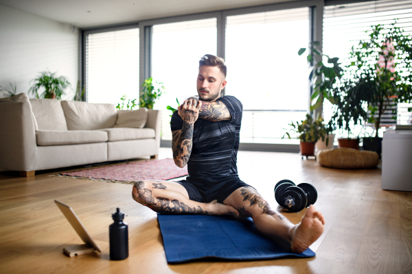 Front view portrait of young man with tablet doing workout exercise indoors at home.