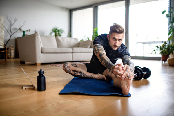 Front view portrait of young man with tablet doing workout exercise indoors at home.