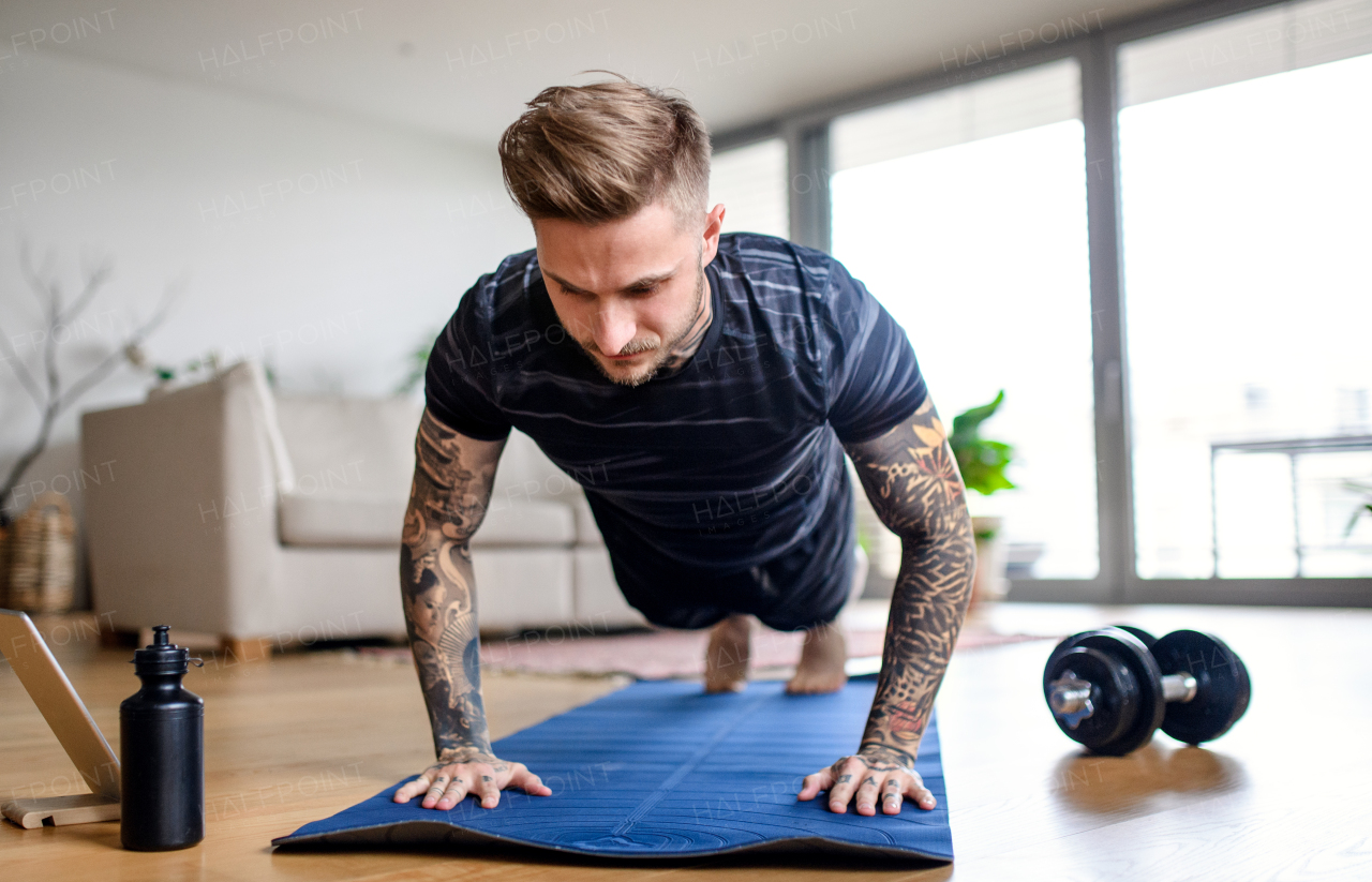 Front view portrait of young man with tablet doing workout exercise indoors at home.