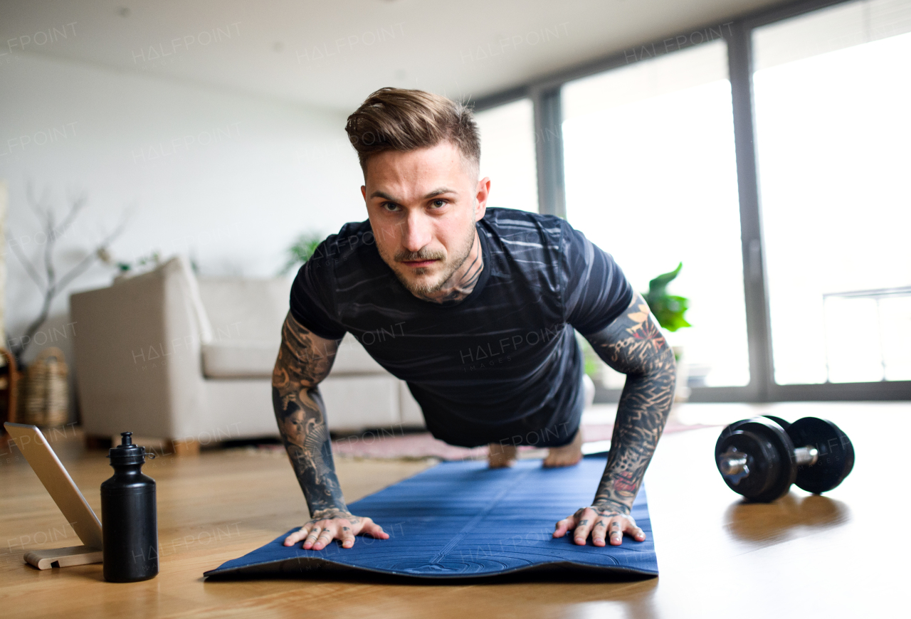 Front view portrait of young man with tablet doing workout exercise indoors at home.