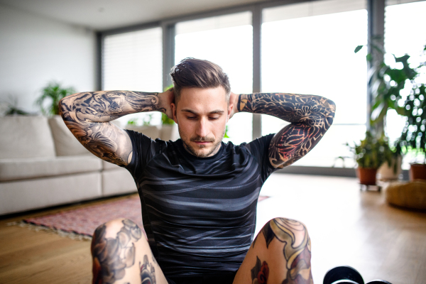 Front view portrait of young man doing workout exercise indoors at home.