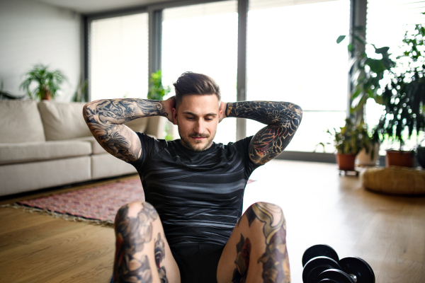 Front view portrait of young man doing workout exercise indoors at home.