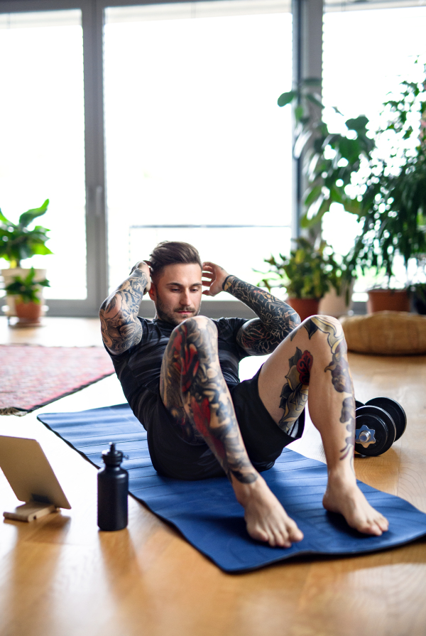 Front view portrait of young man with tablet doing workout exercise indoors at home.