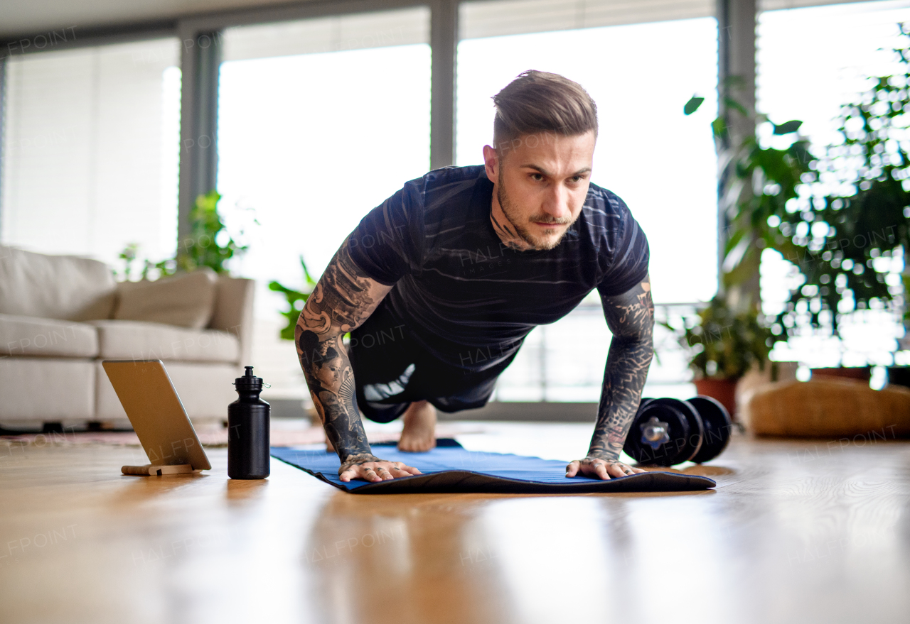 Front view portrait of young man with tablet doing workout exercise indoors at home.