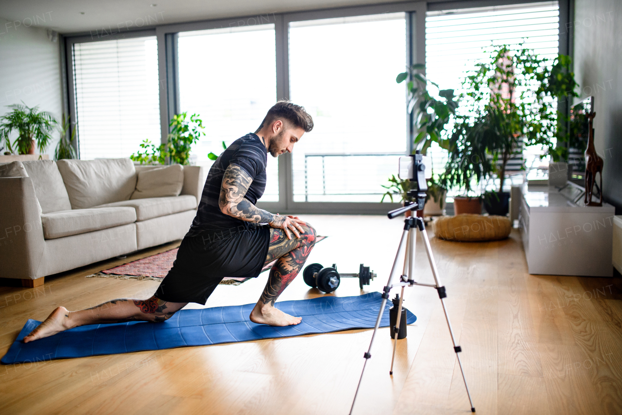 Young man trainer doing online workout exercise indoors at home, using camera.