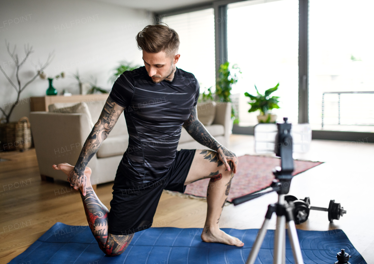 Young man trainer doing online workout exercise indoors at home, using camera.