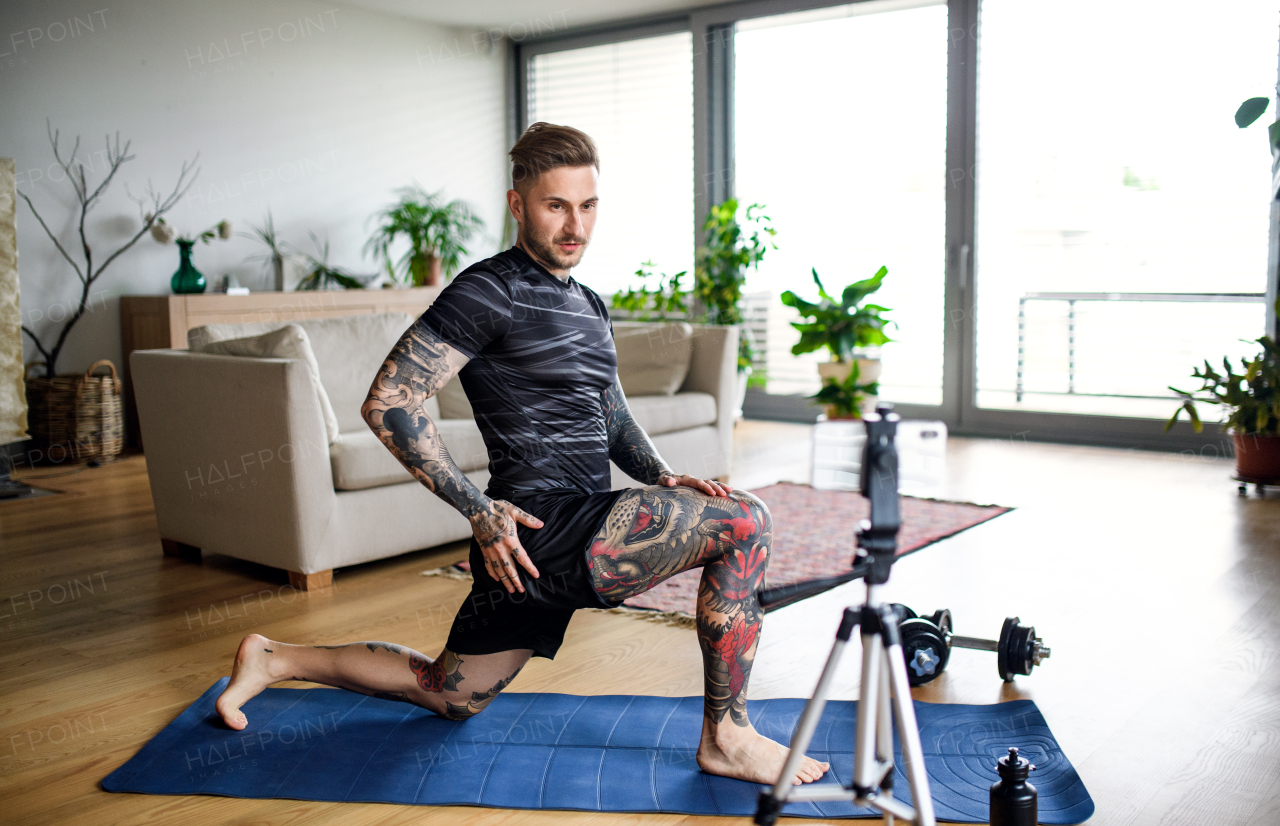 Young man trainer doing online workout exercise indoors at home, using camera.