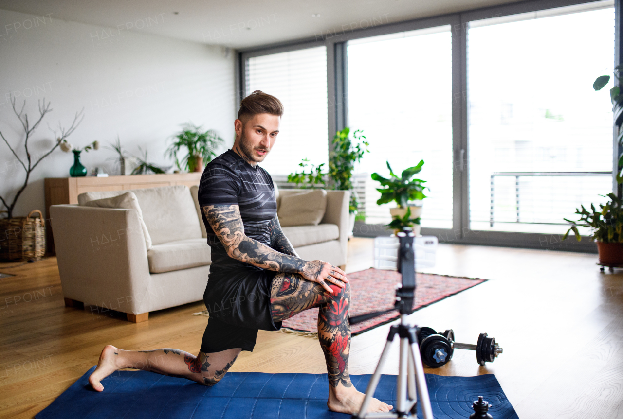 Young man trainer doing online workout exercise indoors at home, using camera.