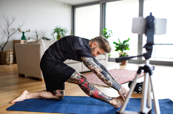 Young man trainer doing online workout exercise indoors at home, using camera.