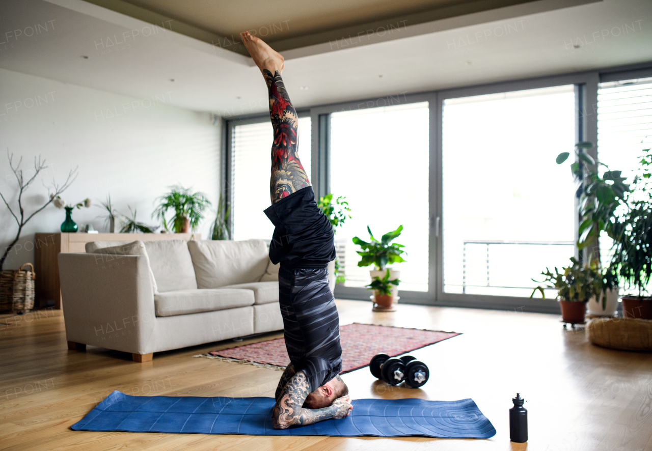 Side view of young man doing workout exercise indoors at home, headstand.