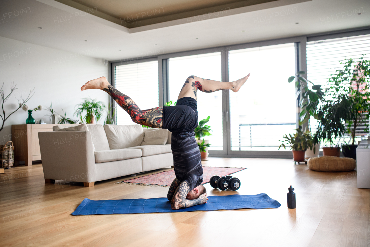 Side view of young man doing workout exercise indoors at home, headstand.