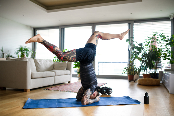 Side view of young man doing workout exercise indoors at home, headstand.