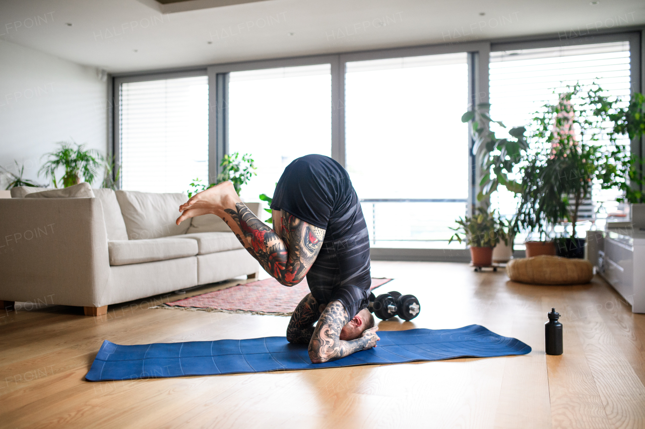 Side view of young man doing workout exercise indoors at home, headstand.