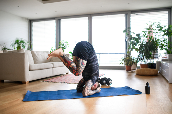 Side view of young man doing workout exercise indoors at home, headstand.