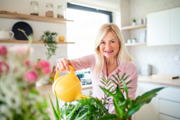 Front view portrait of senior woman watering plants indoors at home.