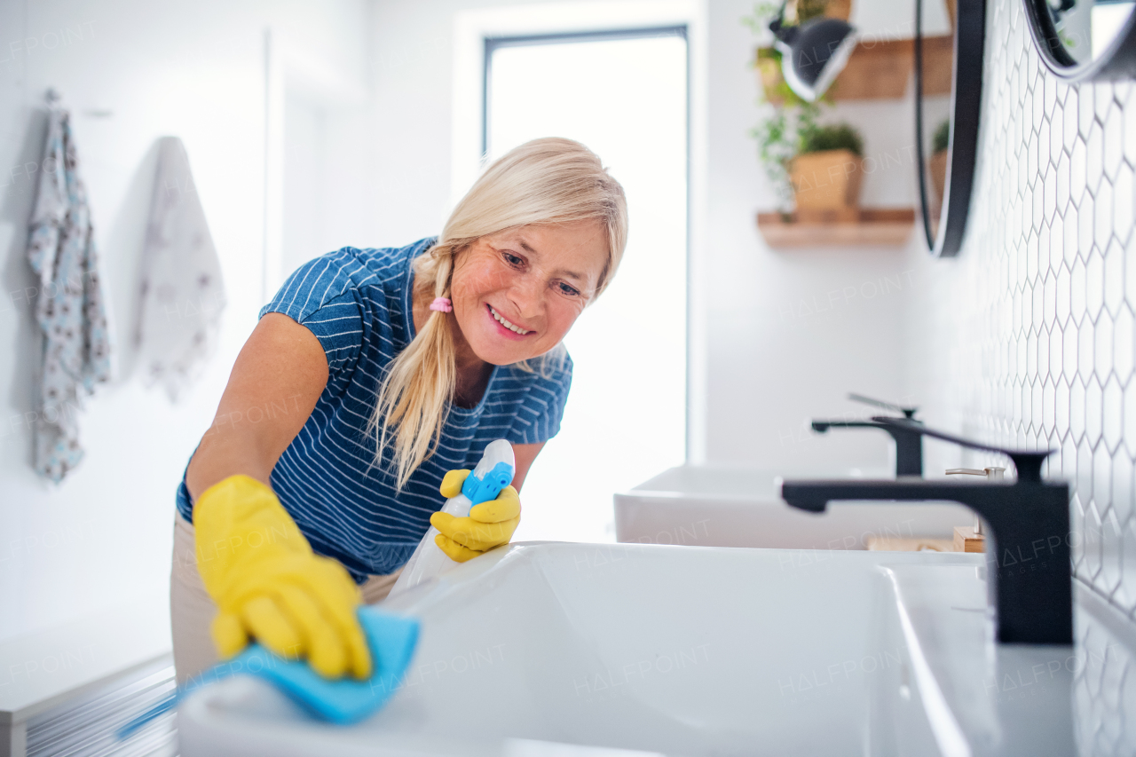 Happy senior woman with gloves cleaning bathroom indoors at home.