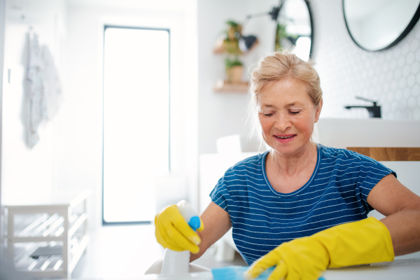 Happy senior woman with gloves cleaning bathroom indoors at home.