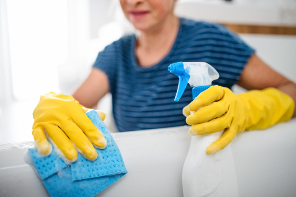 Unrecognizable senior woman with gloves and spraying bottle cleaning indoors at home.