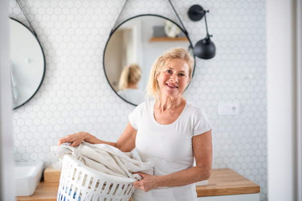 Portrait of senior woman with laundry basket in bathroom indoors at home.