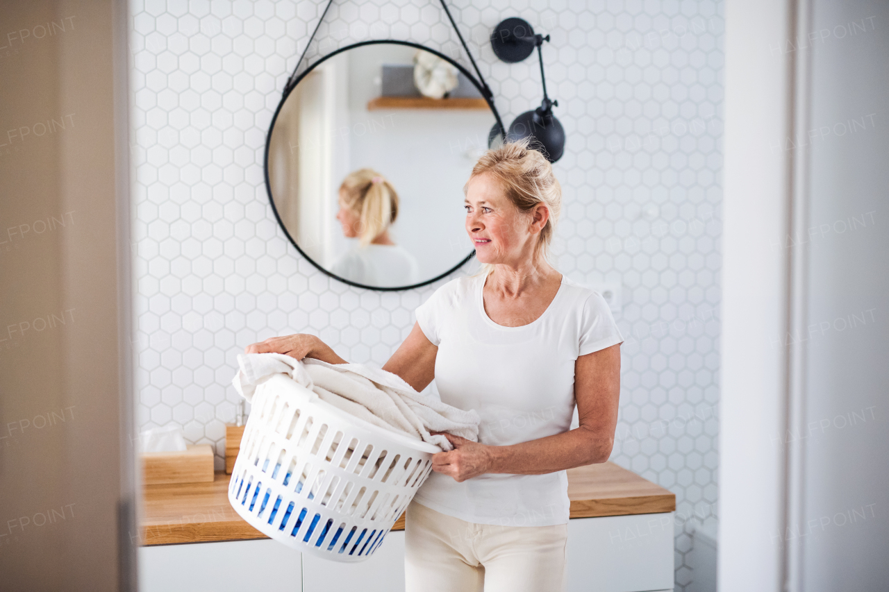 Portrait of senior woman with laundry basket in bathroom indoors at home.