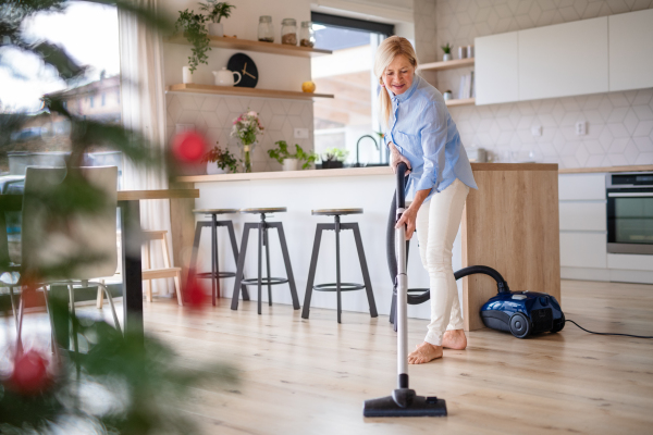 Happy senior woman with vacuum cleaner indoors at home at Christmas time, hoovering.