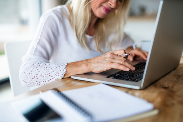 Unrecognizable senior blond woman with laptop indoors in home office, working.