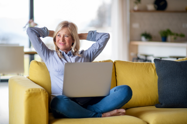 Senior woman with laptop sitting on sofa indoors at home, relaxing.