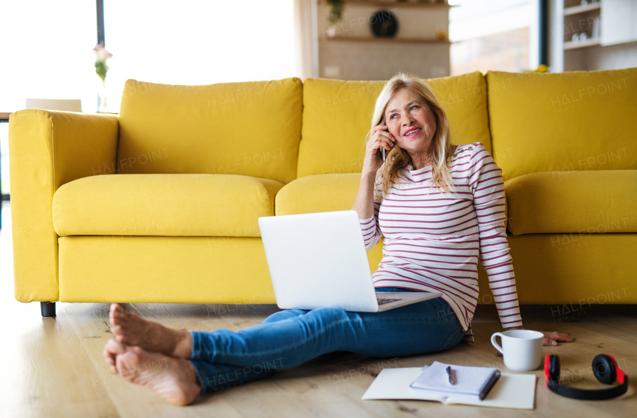 Portrait of senior woman with smartphone and laptop indoors in home office, working.