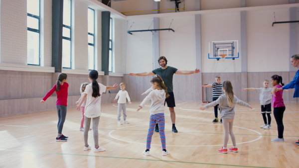 PE teachers and group of elementary students exercising during a class at school gym.