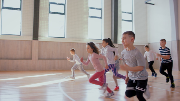 A group of elementary students running during class at school gym.