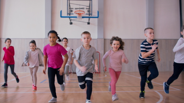 A group of elementary students running during class at school gym.