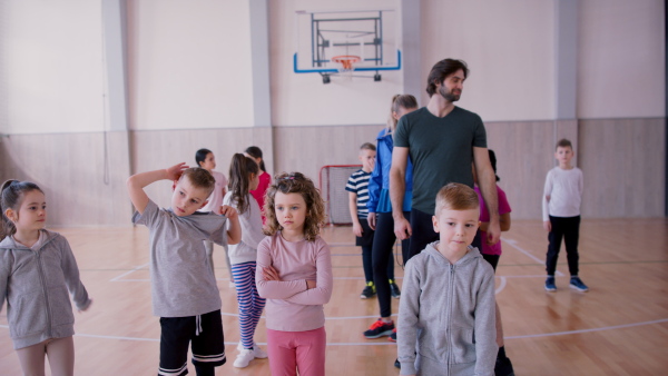 PE teachers and group of elementary students exercising during a class at school gym.