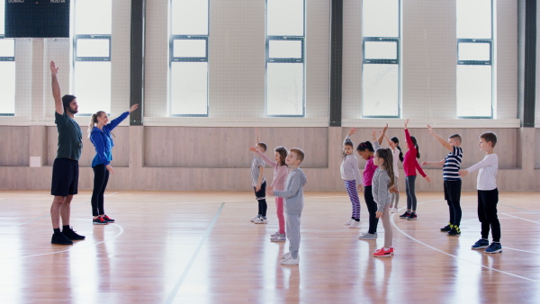 PE teachers and group of elementary students exercising during a class at school gym.