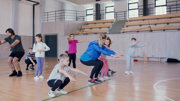 PE teachers and group of elementary students exercising during a class at school gym.