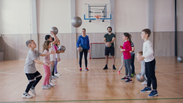 A group of little kids doing physical exercises with fitballs in gym at school.