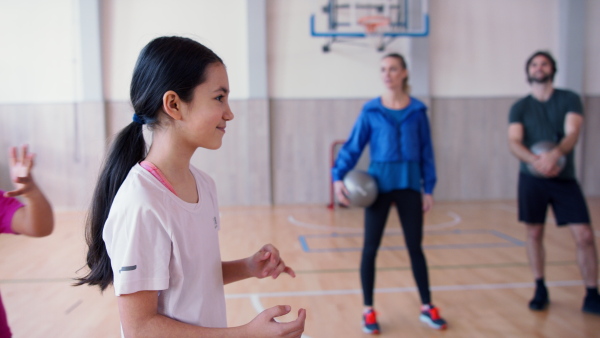 A group of little kids doing physical exercises with fitballs in gym at school.