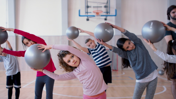 A group of little kids doing physical exercises with fitballs in gym at school.