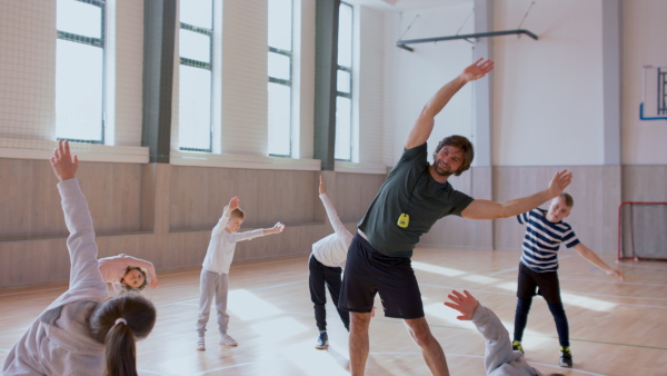 PE teachers and group of elementary students exercising during a class at school gym.