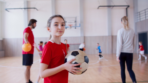 A small multiracial girl standing with ball indoors in gym class, physical education concept