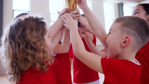 A school sports teammates rising up golden trophy after winning sports indoor competition