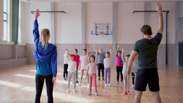 A rear view of PE teachers and group of elementary students exercising during class at school gym.