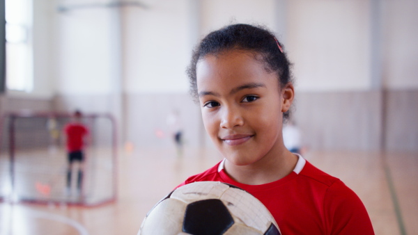 A small multiracial girl standing with ball indoors in gym class, physical education concept