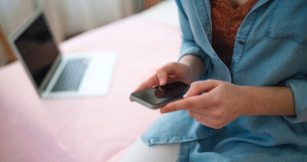 Midsection of young girl with laptop and smartphone sitting indoors, internet abuse concept.