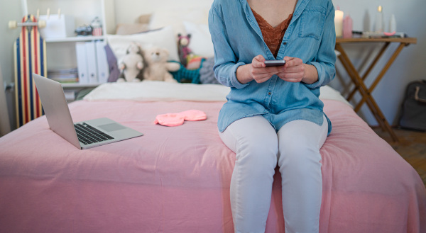 Midsection of young girl with laptop and smartphone sitting indoors, internet abuse concept.