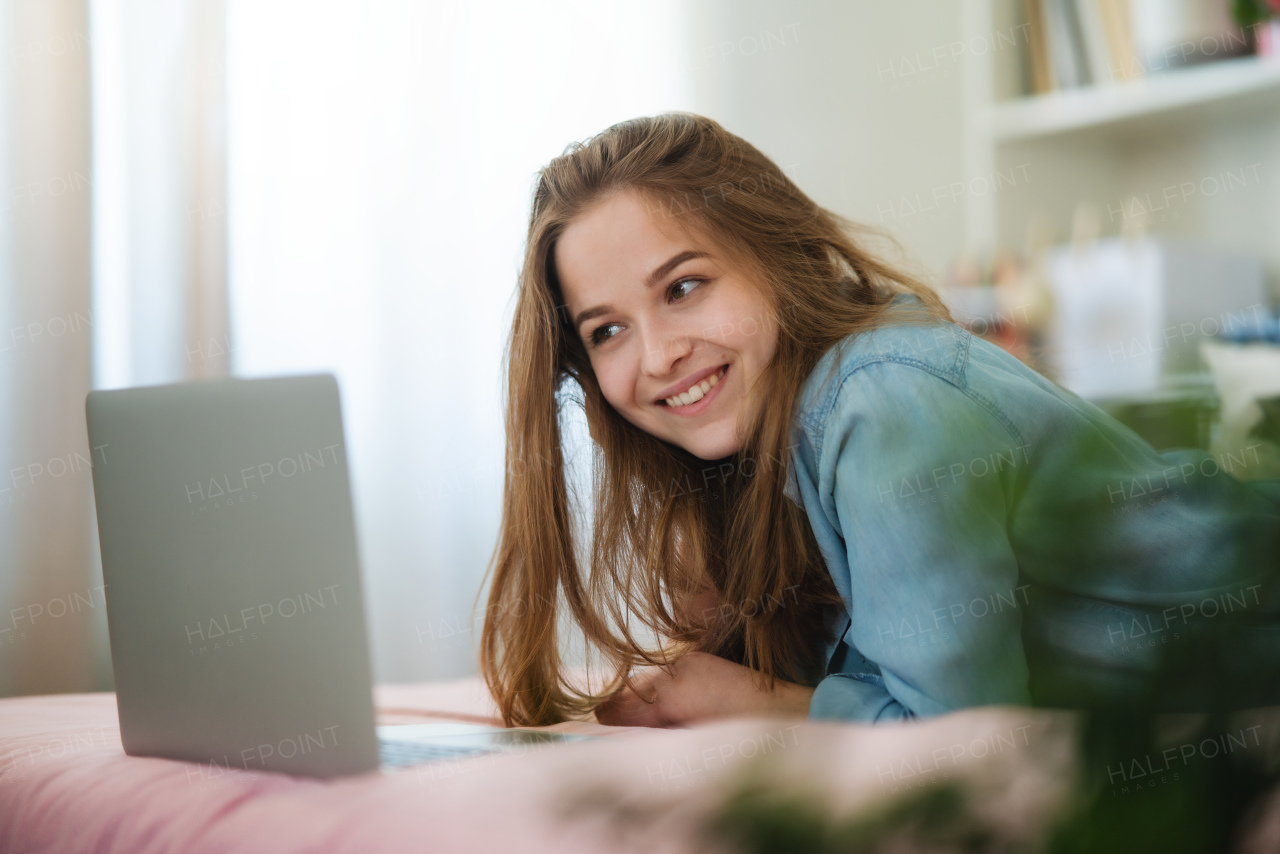 Beautiful happy young girl with laptop lying on bed and smiling, online dating and chatting concept.